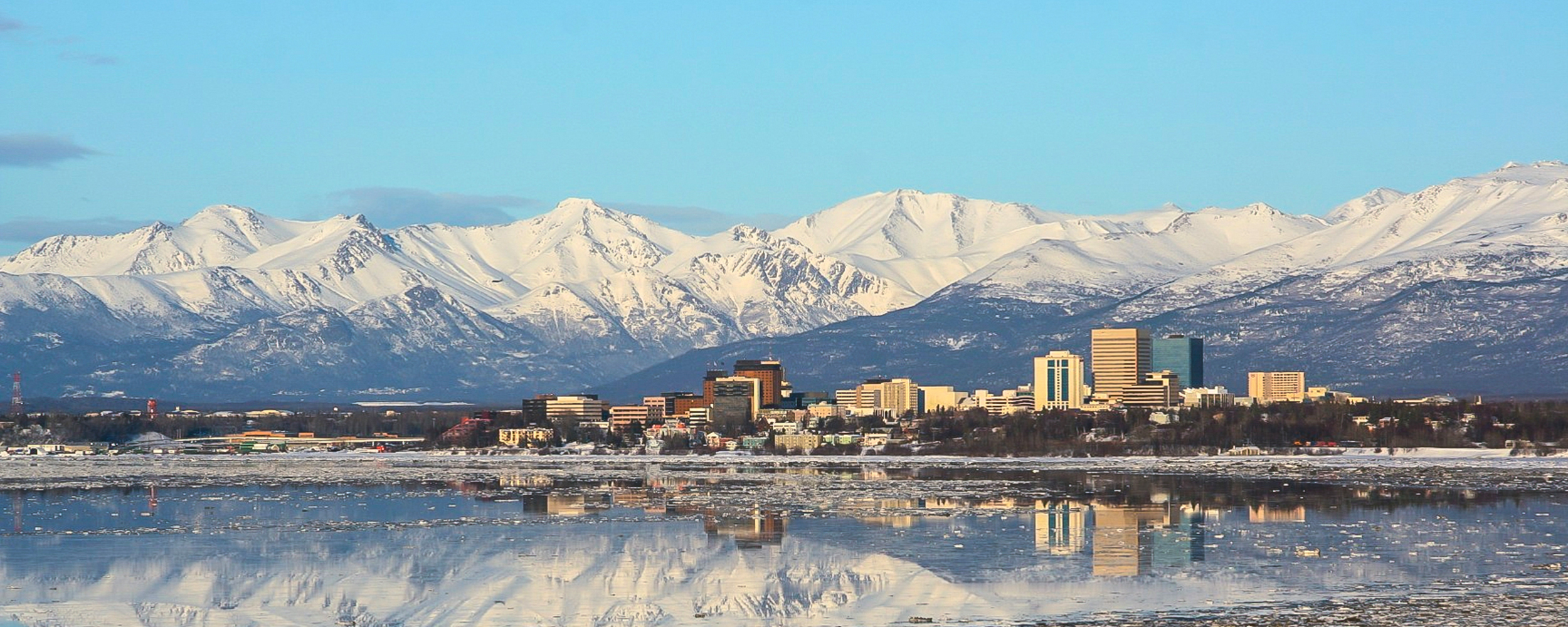 Alaska view from the ocean with the city and snow-covered mountains in the distance.